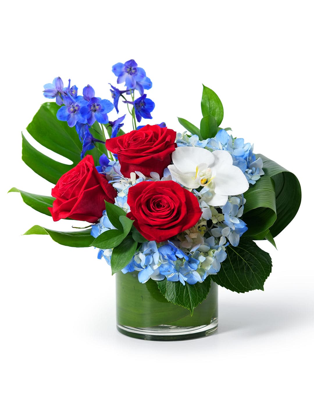 Vibrant floral arrangement featuring red roses, blue hydrangeas, and white orchids in a stylish glass vase.