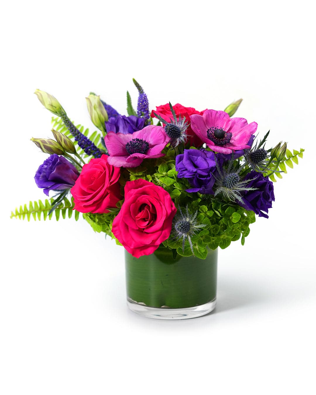 Vibrant mixed flower arrangement featuring pink roses, purple anemones, and lush greenery in a glass vase.