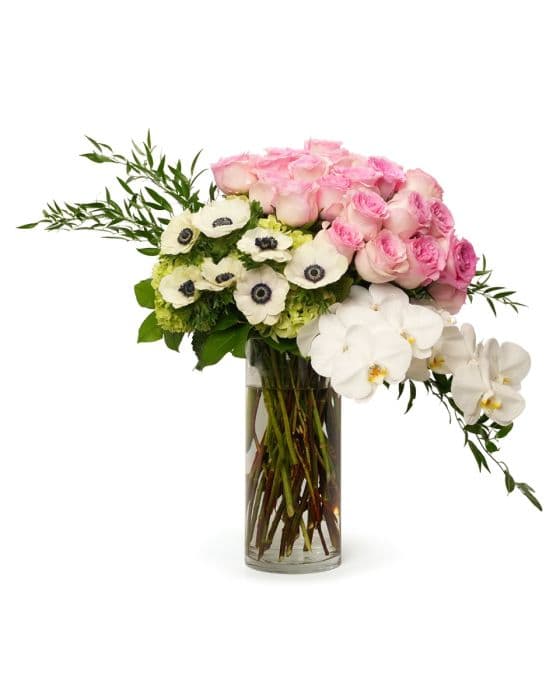 Elegant floral arrangement featuring pink roses, white orchids, and anemones in a clear glass vase. Perfect for gifting.