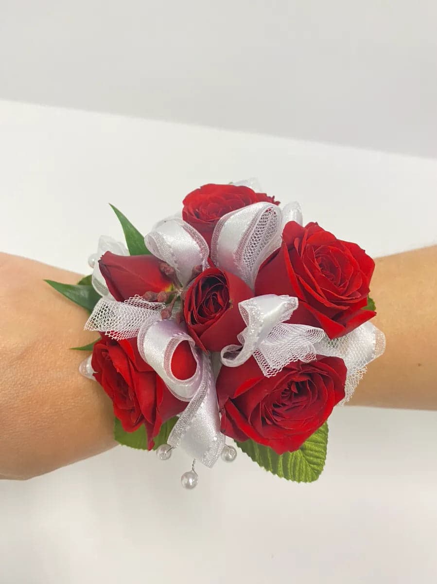 Elegant red rose corsage adorned with white ribbons and decorative pearls, perfect for special occasions.