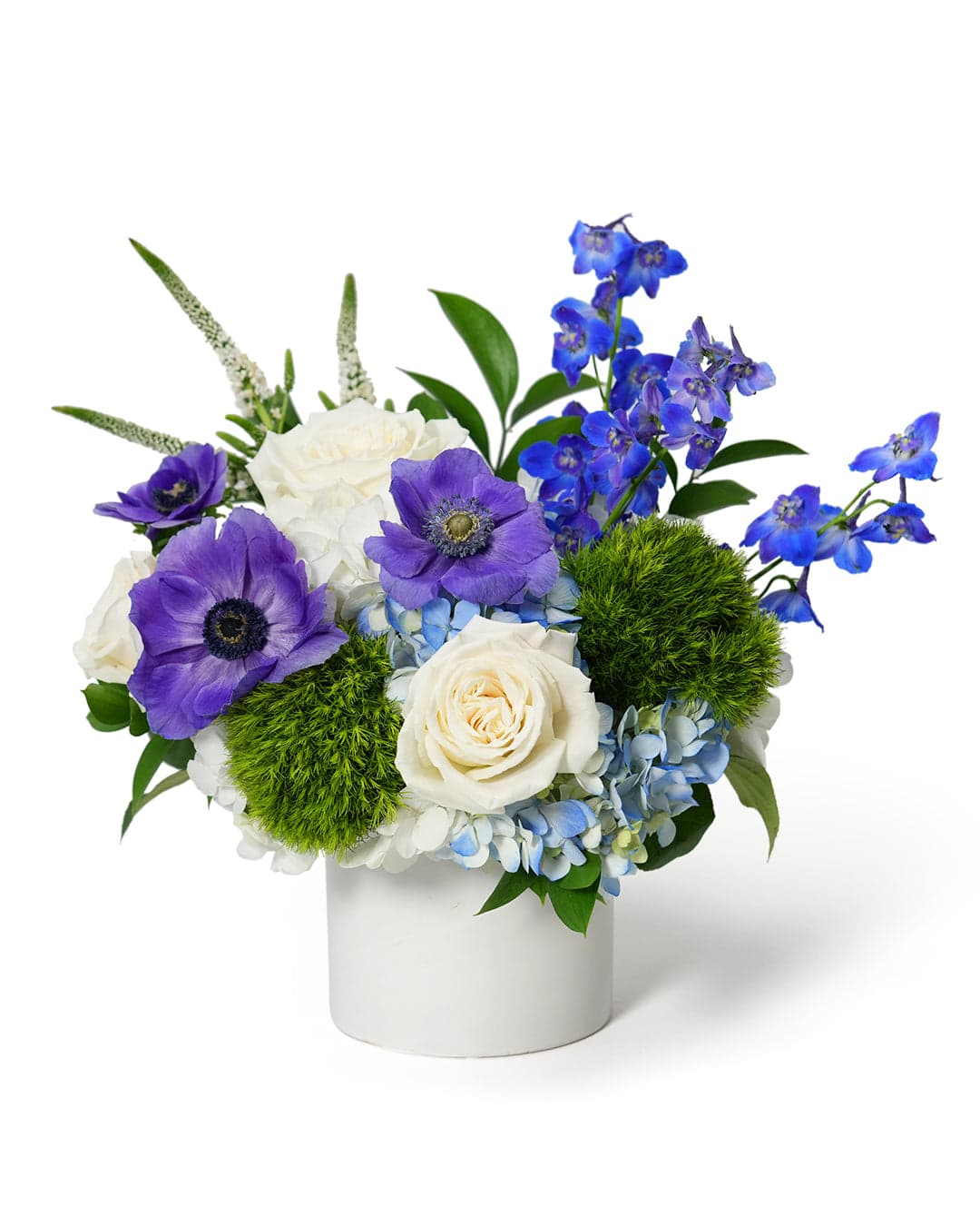 A vibrant floral arrangement featuring purple anemones, white roses, and blue hydrangeas in a sleek white vase.