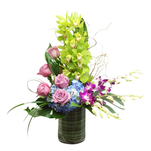 A vibrant floral arrangement featuring pink roses, green orchids, and blue hydrangeas in a stylish glass vase.